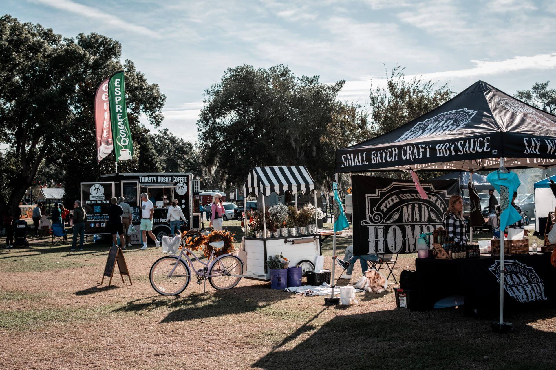 Outdoor food stalls and a food truck at a sunny park market